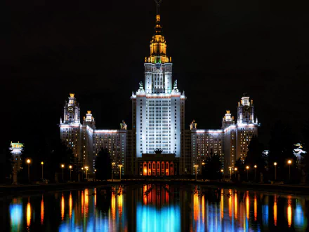 A stunning HD wallpaper featuring Moscow State University at night, with the building's illuminated reflection captured in a calm reflective surface, showcasing the architectural beauty of Moscow, Russia.