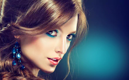 HD wallpaper of a woman model with striking makeup and elegant blue earrings, her face softly lit against a gradient blue background.