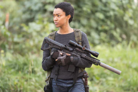 Sonequa Martin-Green from The Walking Dead holds a scoped rifle with silencer, set against a blurred green outdoor background in this 4K Ultra HD PC desktop wallpaper.