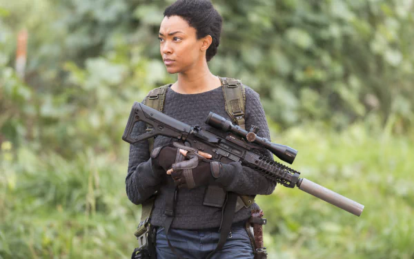 Sonequa Martin-Green from The Walking Dead holds a scoped rifle with silencer, set against a blurred green outdoor background in this 4K Ultra HD PC desktop wallpaper.