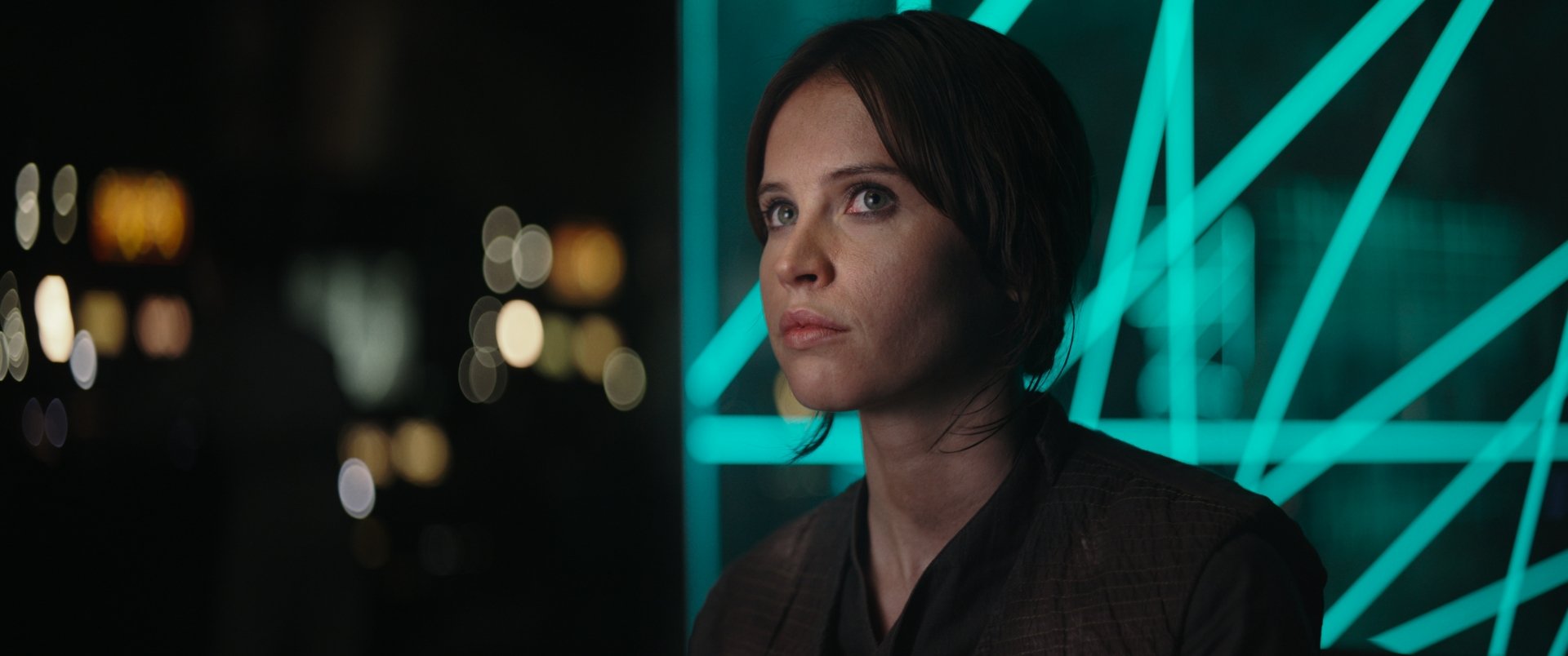 Jyn Erso, portrayed by Felicity Jones, gazes thoughtfully in this HD wallpaper from *Rogue One: A Star Wars Story*, set against a backdrop of striking neon lights.