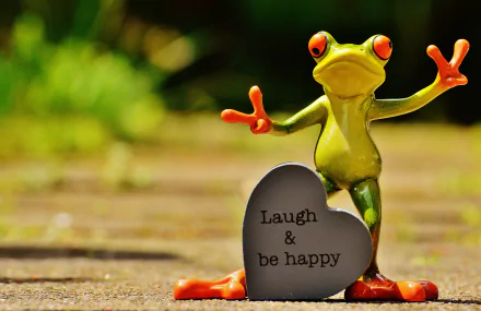 A vibrant frog figurine stands beside a heart-shaped stone that reads Laugh & be happy, set against a lush background in this motivational 4K Ultra HD wallpaper.