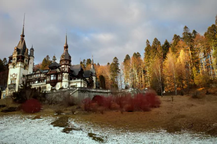 A stunning HD wallpaper of Peles Castle, nestled among autumn trees, with a mix of snow and earth, showcasing the beauty of man-made architecture in a natural setting.