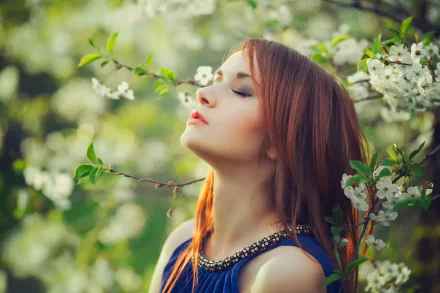 A redheaded woman in a blue top stands with eyes closed among blossoming white flowers on a sunny spring day, creating a serene mood. HD desktop wallpaper and background.
