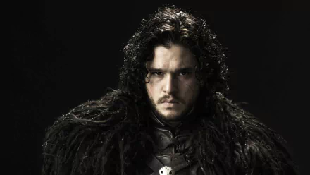 HD desktop wallpaper of Kit Harington as Jon Snow from the TV show Game of Thrones. He is dressed in dark, fur-lined clothing against a black background, with a serious expression on his face.