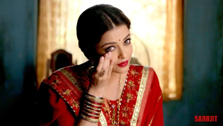 Aishwarya Rai elegantly adorned in a traditional red saree, softly applying makeup, captured in a vibrant setting, highlighting her beauty. Ideal HD wallpaper for desktop backgrounds.