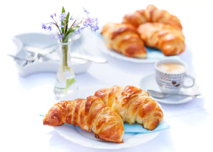 4K Ultra HD desktop wallpaper featuring a breakfast scene with golden croissants, a cup of coffee, and a small vase with purple flowers on a bright white table.
