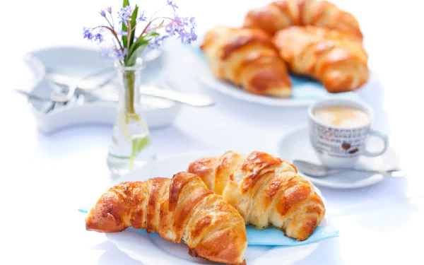 4K Ultra HD desktop wallpaper featuring a breakfast scene with golden croissants, a cup of coffee, and a small vase with purple flowers on a bright white table.