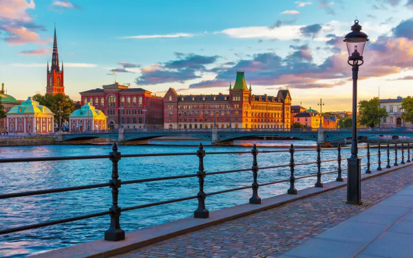 HD desktop wallpaper of Stockholm, Sweden featuring a man-made riverside promenade with historic buildings and a lamppost under a colorful sky.