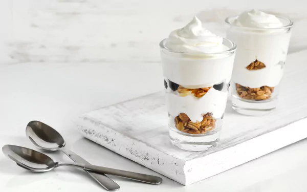 4K Ultra HD wallpaper featuring two glasses of creamy dessert layered with nuts on a white marble surface, accompanied by two spoons.