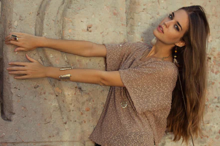 A Spanish woman named Clara Alonso poses elegantly against a textured wall, showcasing her long hair and stylish outfit in this 4K Ultra HD desktop wallpaper.