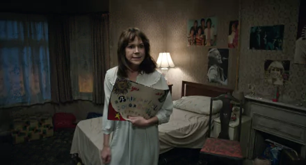 A tense scene from The Conjuring 2 featuring a woman in a nightgown holding a Ouija board in a dimly lit room, adding an eerie atmosphere to your HD desktop wallpaper.