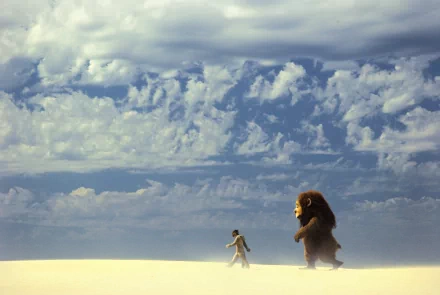 Where the Wild Things Are movie scene: boy walks across bright sand with a large furry creature beneath dramatic clouded sky — 2K Quad HD PC desktop wallpaper/background.