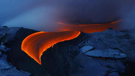 A stunning HD wallpaper featuring flowing lava from a volcano, illuminated in vibrant orange against a dark, rocky landscape, showcasing the raw power of nature.