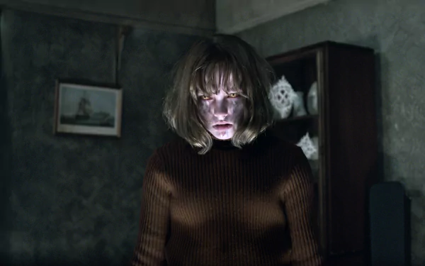 A haunting scene from *The Conjuring 2*, featuring Sterling Jerins. The image depicts a girl with a ghostly expression, illuminated in a dimly lit, eerie setting.