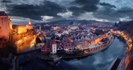 HD PC desktop wallpaper: Czech Republic cityscape — historic man-made riverside town with red-tiled roofs, church spire and winding river glowing under dramatic dusk skies.
