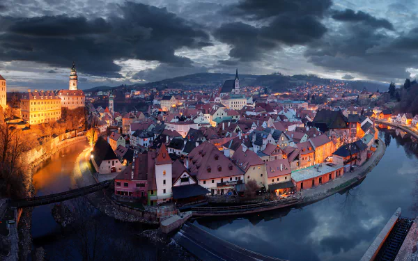HD PC desktop wallpaper: Czech Republic cityscape — historic man-made riverside town with red-tiled roofs, church spire and winding river glowing under dramatic dusk skies.