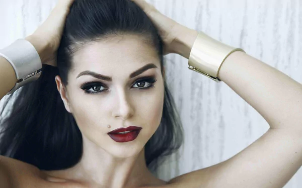 HD desktop wallpaper: close-up portrait of a brunette singer with brown eyes and bold lipstick, hands in her hair and a confident, music-artist expression.