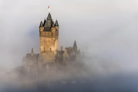 Cochem Castle in Germany emerges through thick fog, showcasing its historic towers and medieval architecture in an atmospheric HD desktop wallpaper.