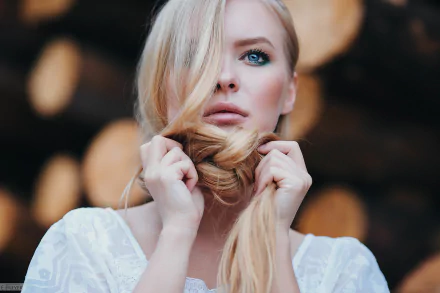 HD desktop wallpaper of a blonde woman with striking blue eyes, holding her braided hair close to her face in a soft, blurred background.