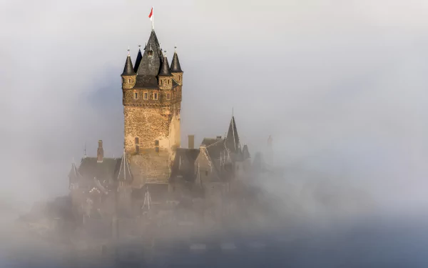 Cochem Castle in Germany emerges through thick fog, showcasing its historic towers and medieval architecture in an atmospheric HD desktop wallpaper.