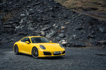 Yellow Porsche 911 Carrera sports car parked on rocky terrain, showcased in sharp 4K Ultra HD resolution for PC desktop wallpaper and background.
