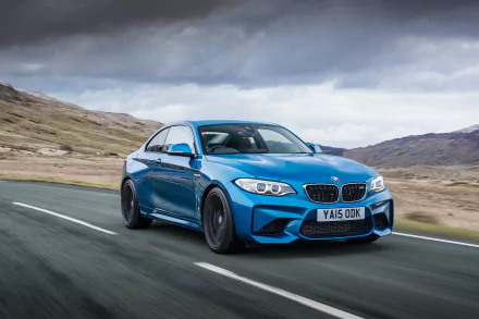 Blue BMW M2 driving on a scenic road under a cloudy sky, captured in high-resolution 4K Ultra HD for a striking PC desktop wallpaper background.