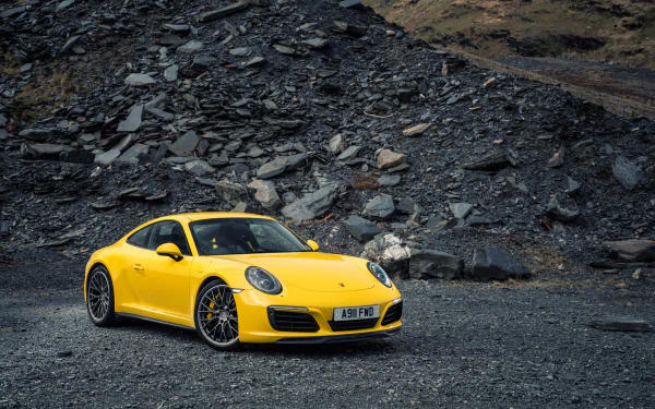 Yellow Porsche 911 Carrera sports car parked on rocky terrain, showcased in sharp 4K Ultra HD resolution for PC desktop wallpaper and background.