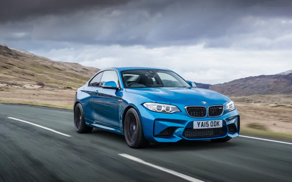 Blue BMW M2 driving on a scenic road under a cloudy sky, captured in high-resolution 4K Ultra HD for a striking PC desktop wallpaper background.