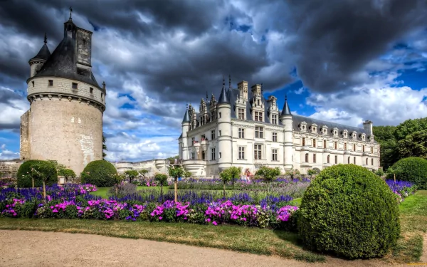 View of the Château de Chenonceau in France, showcasing its historic architecture and vibrant garden under a dramatic cloudy sky, captured in HD for a PC desktop wallpaper.