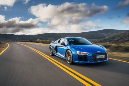 A stunning Audi R8 V10 in vibrant blue speeds along a winding road, surrounded by scenic hills and dramatic clouds, serving as an impressive HD desktop wallpaper.