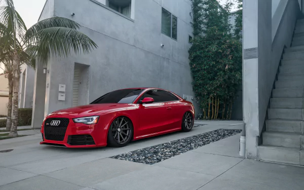 HD desktop wallpaper featuring a sleek red Audi A5 parked in a modern, minimalist courtyard with concrete and greenery.