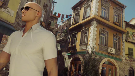 A sleek bald man in sunglasses stands confidently in a vibrant street setting, showcasing an HD wallpaper inspired by Agent 47 from the video game Hitman (2016).