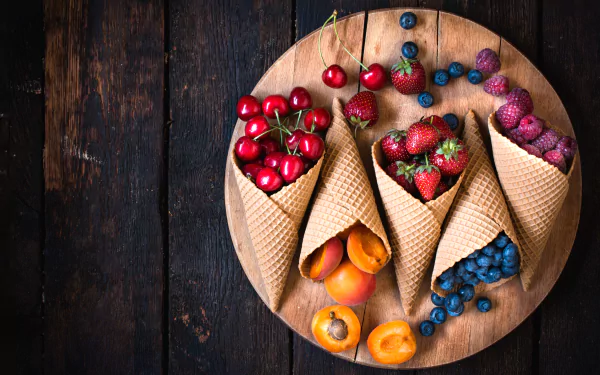 A 4K Ultra HD desktop wallpaper featuring fresh peaches, cherries, strawberries, raspberries, and blueberries arranged in waffle cones on a wooden board.