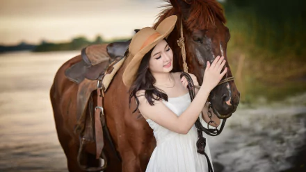 Asian woman in a white dress and hat standing beside a brown horse near a body of water, smiling with eyes closed. Background shows a serene outdoor setting. HD desktop wallpaper.