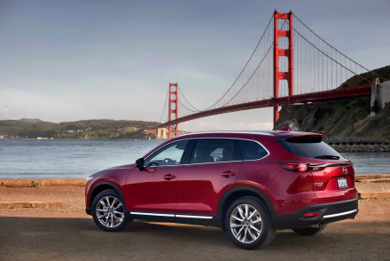 A red Mazda CX-9 SUV parked by the waterfront with the Golden Gate Bridge in the background, featured as an HD PC desktop wallpaper.