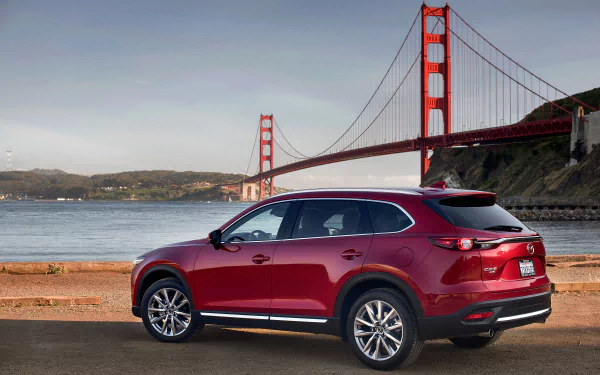A red Mazda CX-9 SUV parked by the waterfront with the Golden Gate Bridge in the background, featured as an HD PC desktop wallpaper.