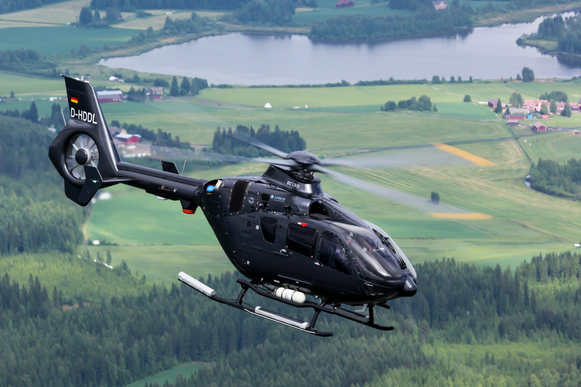 A sleek black Eurocopter EC135 helicopter in flight over a lush green landscape with rivers, captured as an HD PC desktop wallpaper background.