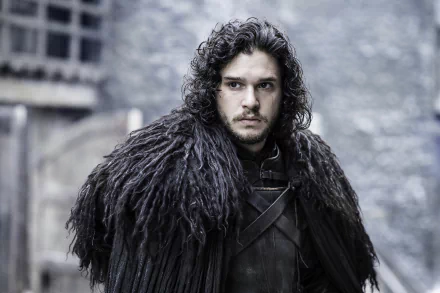Jon Snow, portrayed by Kit Harington in Game of Thrones, stands in a dramatic pose wearing his signature dark fur cloak, set against a somber background of the show's medieval landscape.