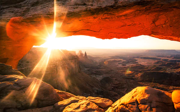 Sunrise illuminates Utah’s Mesa Arch, casting warm light over the vast horizon and rugged landscape in this stunning 4K Ultra HD nature wallpaper.
