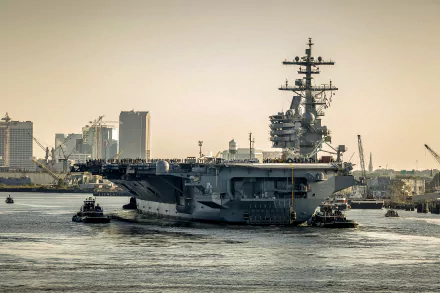 The USS George H.W. Bush (CVN-77) aircraft carrier, a powerful military warship, navigates a harbor with city buildings in the background.