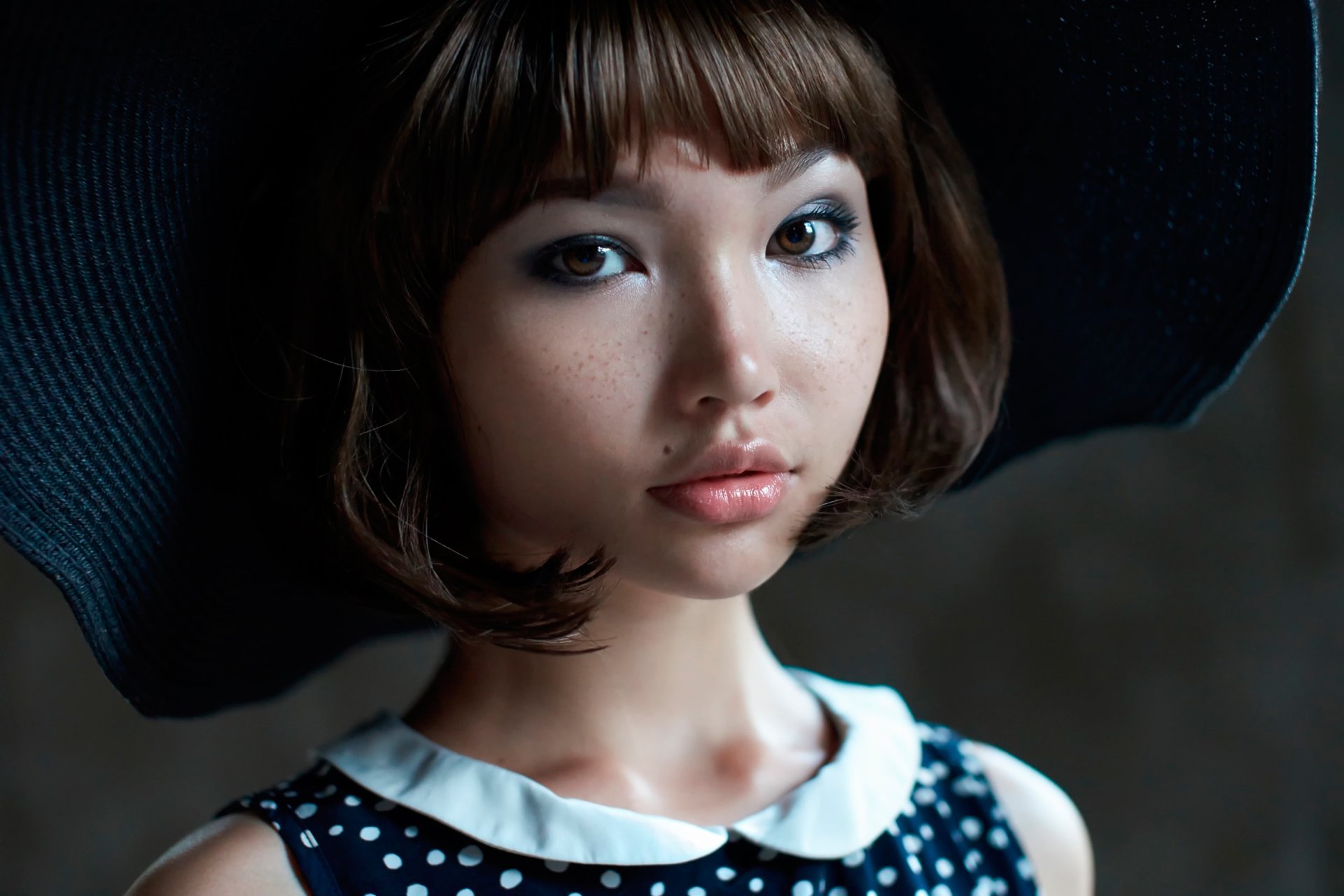 HD desktop wallpaper of a brunette woman model with brown eyes, freckles, and a large black hat, featuring a close-up of her face against a dark background.
