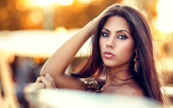 Brunette woman with striking brown eyes poses against a warm bokeh background, captured in high-definition for a PC desktop wallpaper.