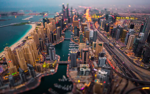 A tilt-shift aerial view of Dubai’s skyscrapers and cityscape along the waterfront, showcasing the vibrant urban skyline of the United Arab Emirates at dusk.