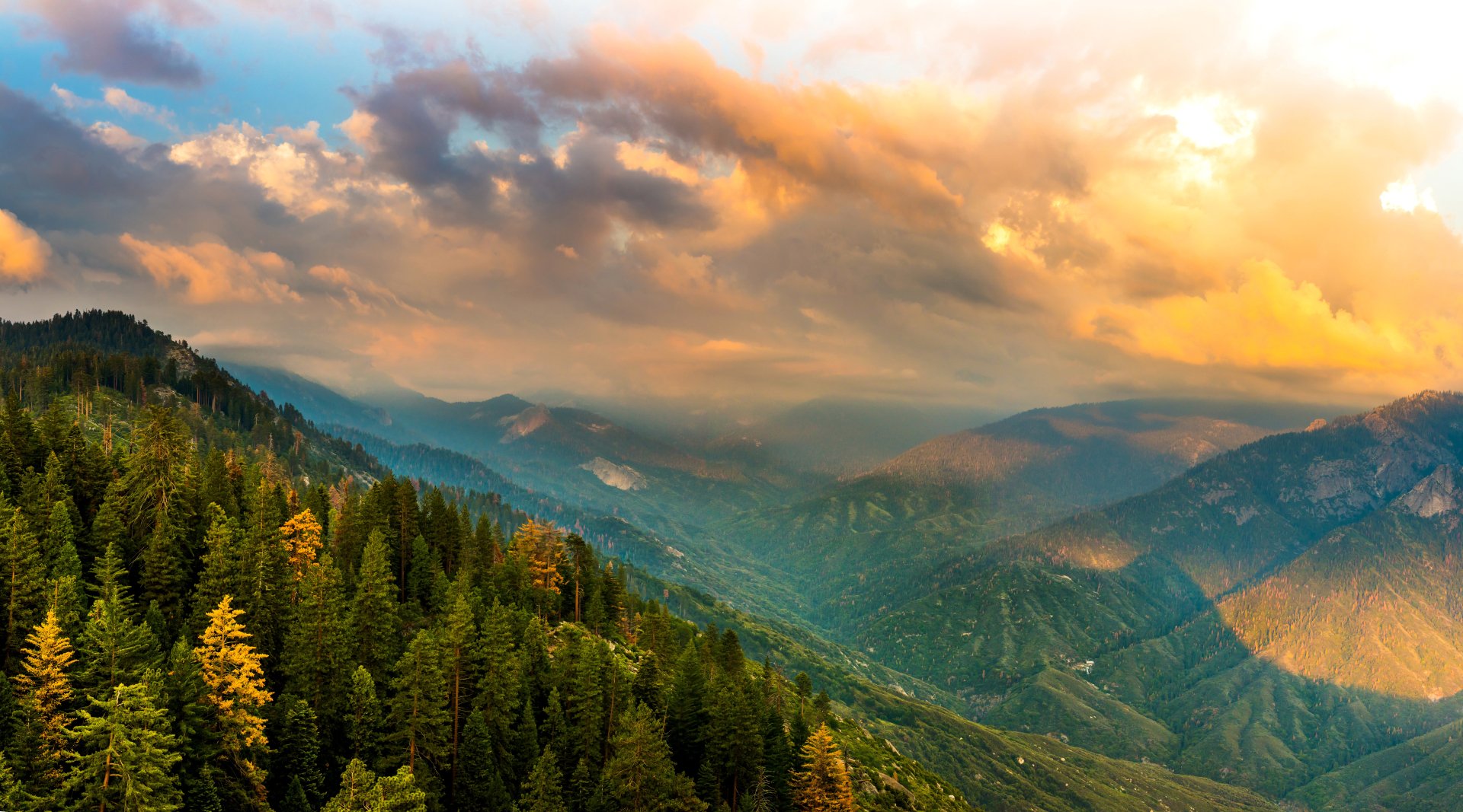 A 4K Ultra HD desktop wallpaper showcasing a vibrant mountain valley landscape with dense forest under dramatic cloud-filled skies.