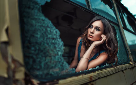 A brunette woman with brown eyes and a contemplative expression leans on the broken window frame of an old vehicle, captured in an HD desktop wallpaper style.