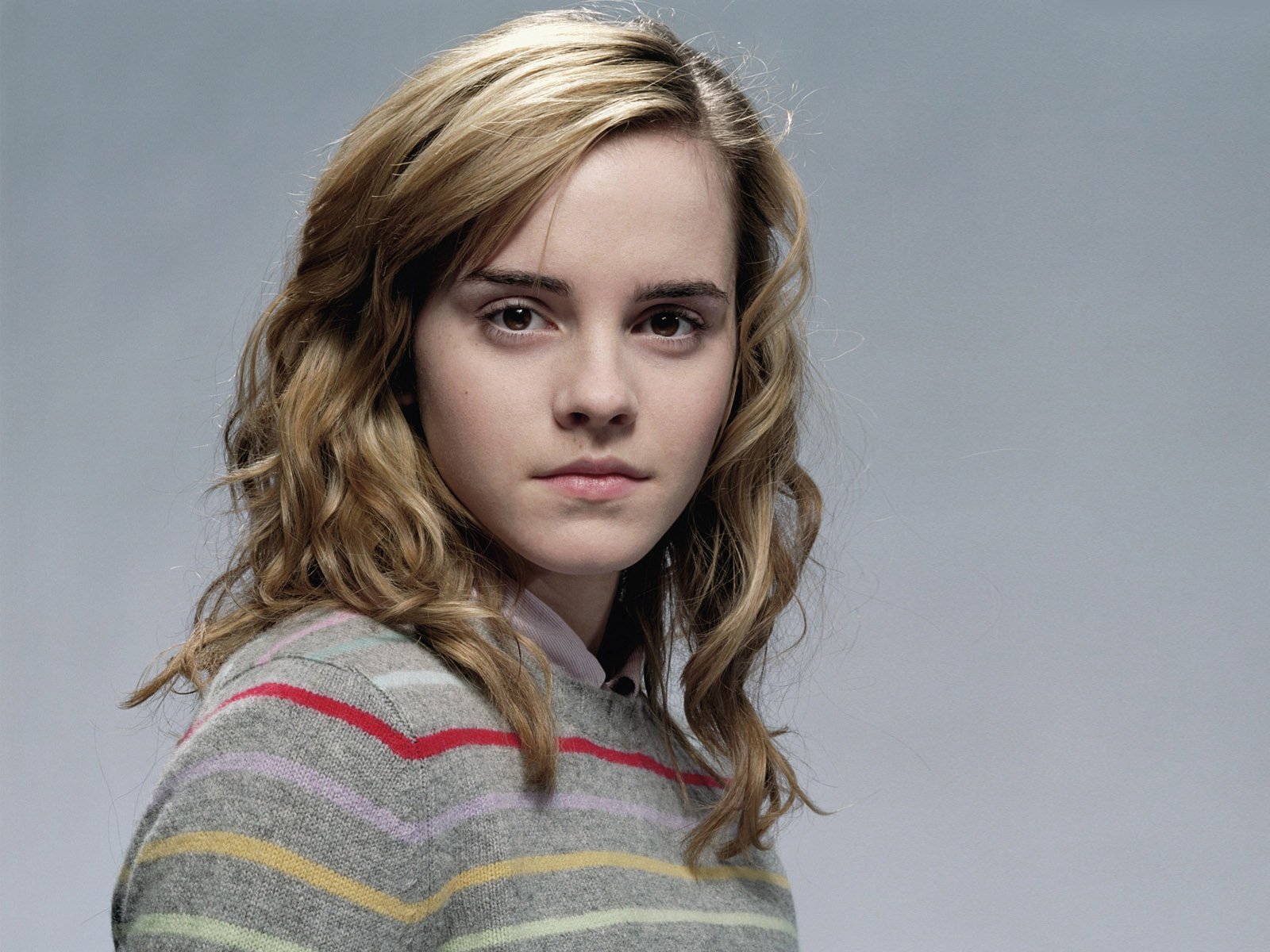 HD desktop wallpaper featuring a close-up portrait of celebrity Emma Watson with a neutral expression and soft lighting against a plain background.