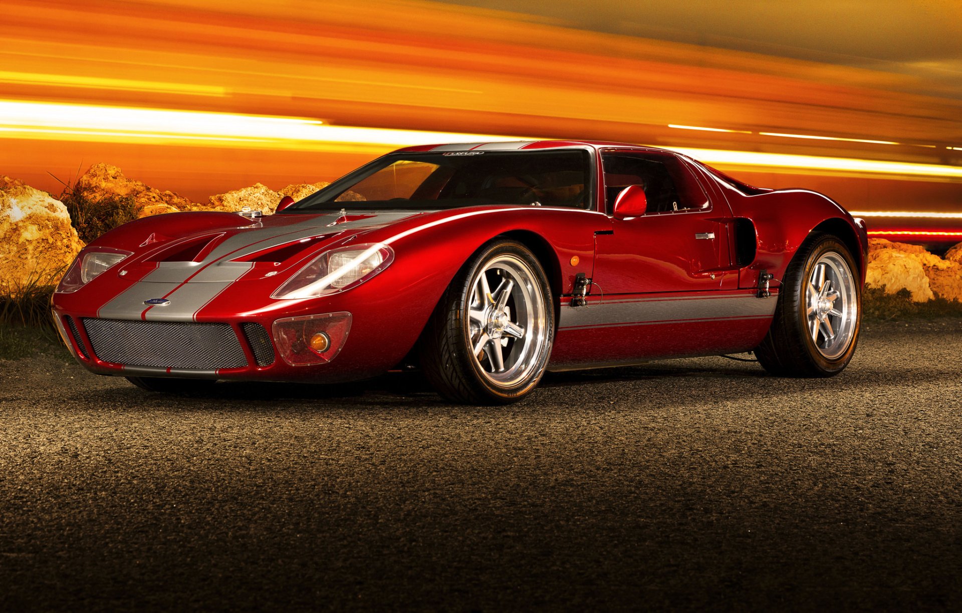 A red Ford GT40 supercar parked on a road with a dynamic, fiery orange sky in the background, captured in HD for a sleek PC desktop wallpaper.