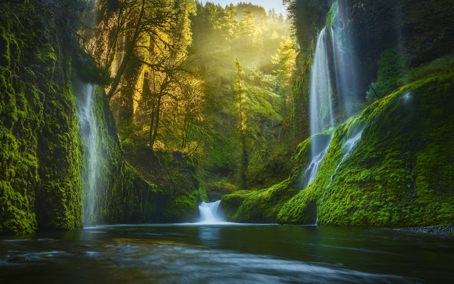HD PC desktop wallpaper showcasing a lush green forest with cascading waterfalls and sunlight filtering through dense foliage over a tranquil pool.
