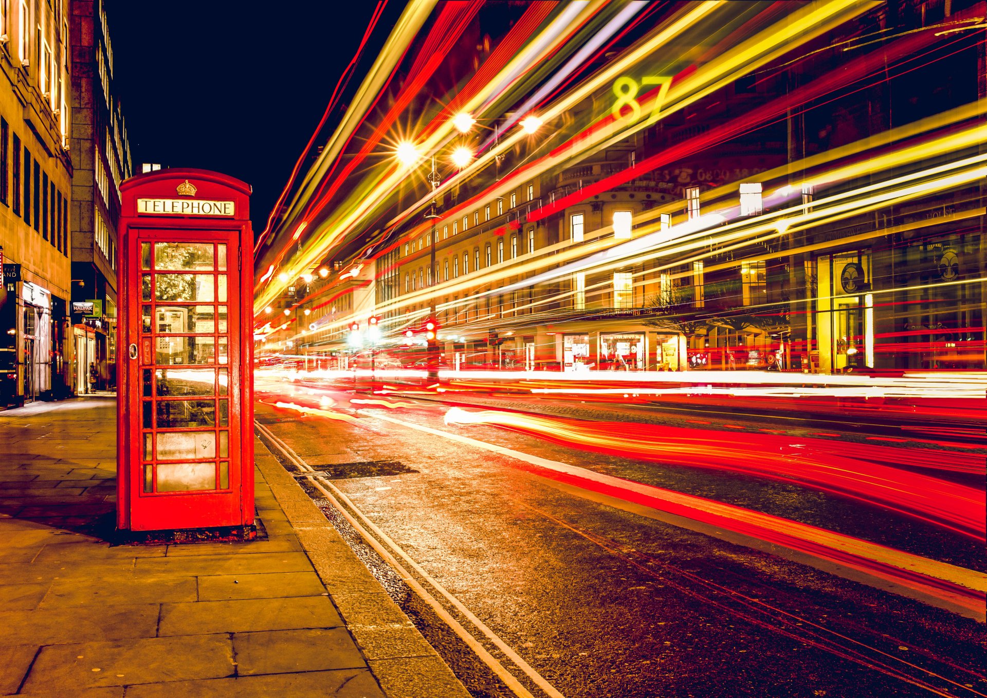 A vibrant 4K Ultra HD night scene of a classic red telephone booth illuminated by streetlights, with dynamic light trails captured through time-lapse photography.